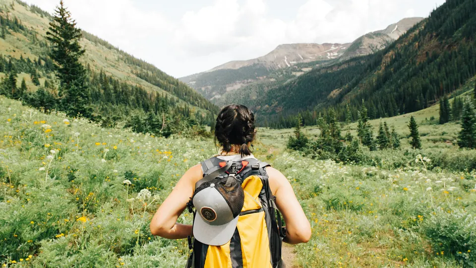 Wanderin mit Rucksack auf einem Weg durch ein grünes Bergtal