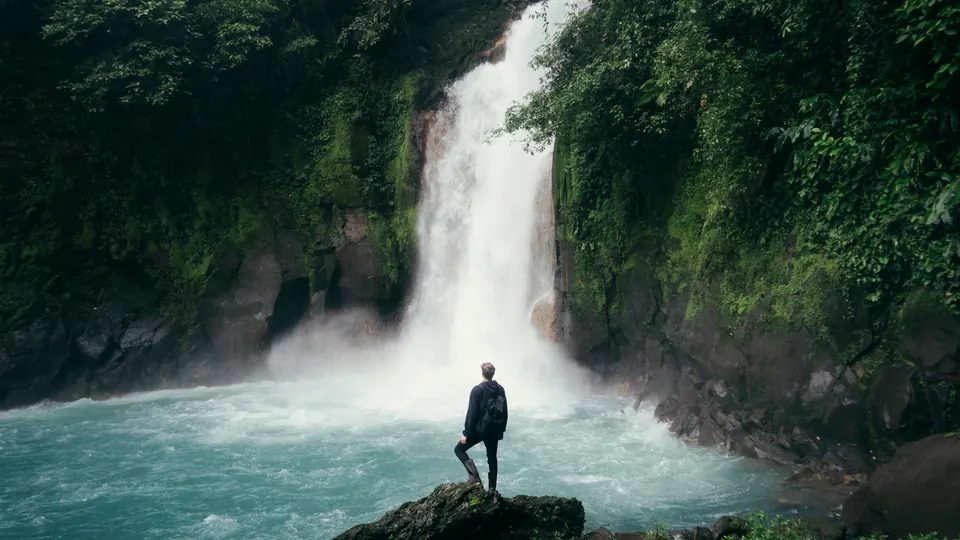 Ein Reisender vor einem Wasserfall und türkisfarbenem Wasser